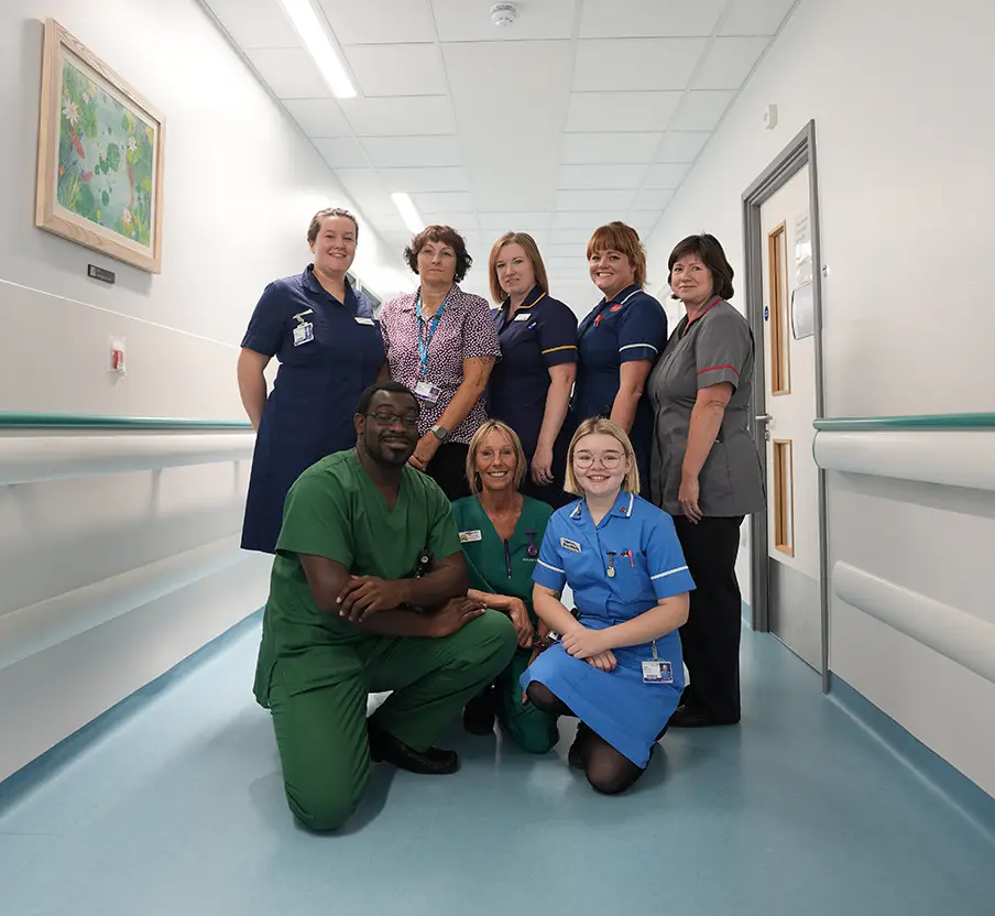 A group of RCHT NHS staff smiling for a photograph in a ward corridor